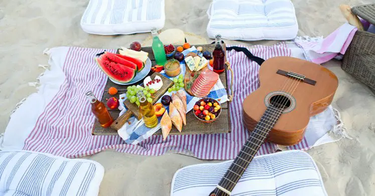 Awesome boho beach picnic with fruits, bread, drinks, and a guitar