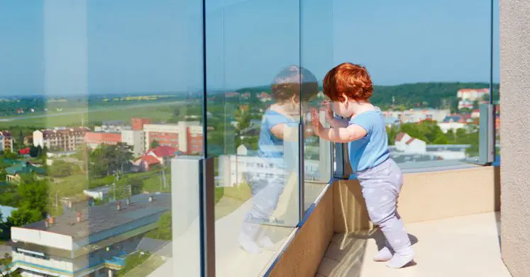 Child leaning at safe glass railing on balcony