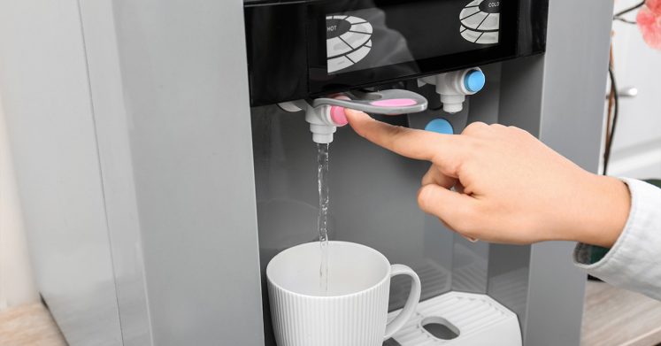 A person is filling a cup from an instans hot water dispenser